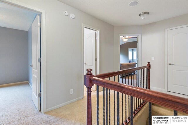 hallway featuring an upstairs landing, light colored carpet, and baseboards