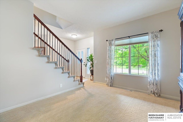 carpeted entrance foyer featuring stairway and baseboards
