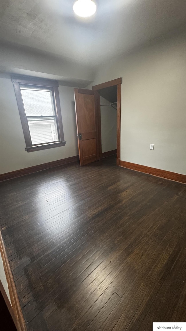 unfurnished bedroom featuring baseboards, dark wood-type flooring, and a closet