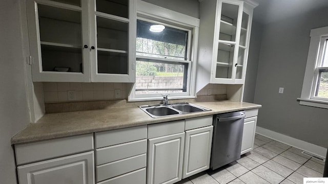kitchen with dishwasher, a sink, decorative backsplash, light tile patterned floors, and glass insert cabinets