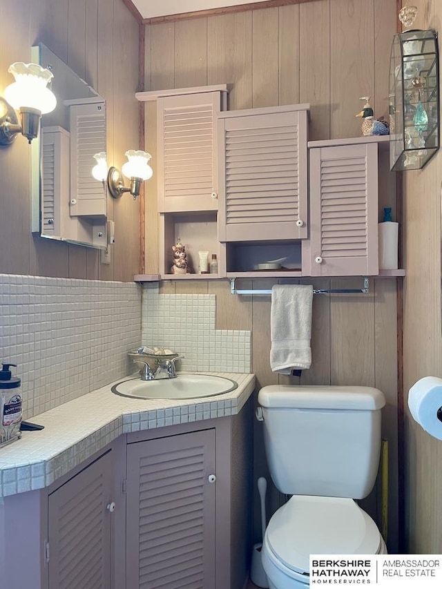 1200 H St, Pawnee City, NE 68420 - half bath with decorative backsplash, toilet, vanity, and wood walls