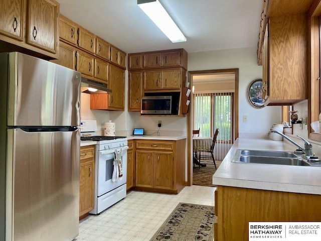 1200 H St, Pawnee City, NE 68420 - kitchen with stainless steel appliances, under cabinet range hood, a sink, brown cabinetry, and light countertops