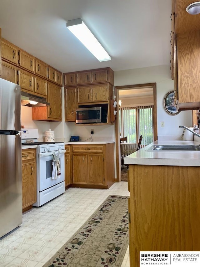 1200 H St, Pawnee City, NE 68420 - kitchen with appliances with stainless steel finishes, a sink, under cabinet range hood, brown cabinetry, and light countertops