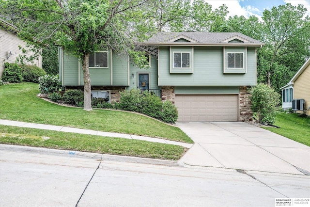 split foyer home featuring an attached garage, driveway, central AC, a front yard, and stone siding
