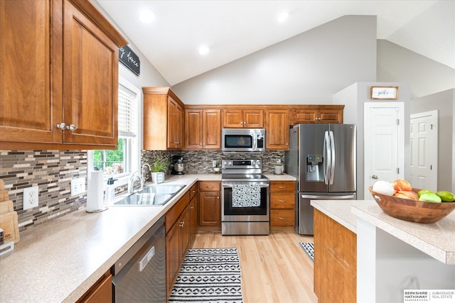 kitchen featuring appliances with stainless steel finishes, a sink, light countertops, light wood-type flooring, and high vaulted ceiling