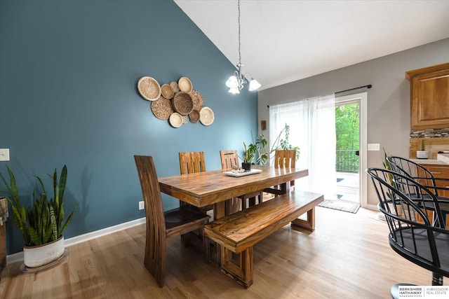 dining area featuring high vaulted ceiling, light wood finished floors, a chandelier, and baseboards