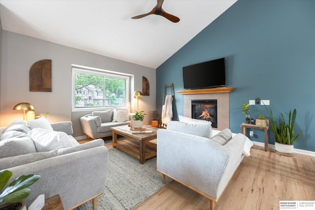 living room with ceiling fan, wood finished floors, a fireplace, high vaulted ceiling, and baseboards