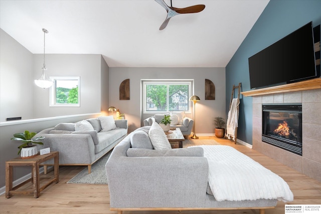 living room with lofted ceiling, healthy amount of natural light, a tiled fireplace, a ceiling fan, and light wood-style floors