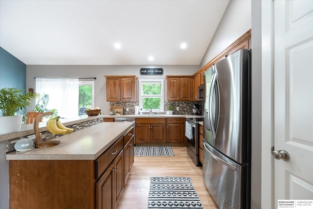 kitchen featuring appliances with stainless steel finishes, a sink, light wood-type flooring, tasteful backsplash, and brown cabinetry