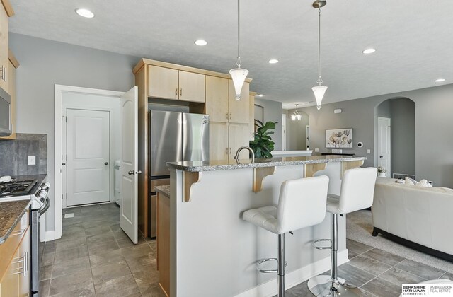 7211 S 174th St, Omaha, NE 68136 - kitchen featuring stainless steel appliances, light brown cabinetry, arched walkways, recessed lighting, and a kitchen breakfast bar