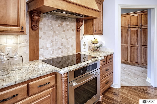 3400 Firethorn Ter, Lincoln, NE 68520 - kitchen with stainless steel oven, custom range hood, black electric cooktop, tasteful backsplash, and light stone counters
