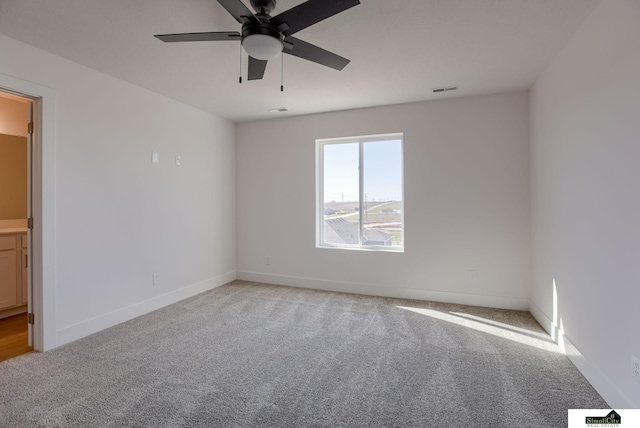 spare room featuring light colored carpet, ceiling fan, and baseboards