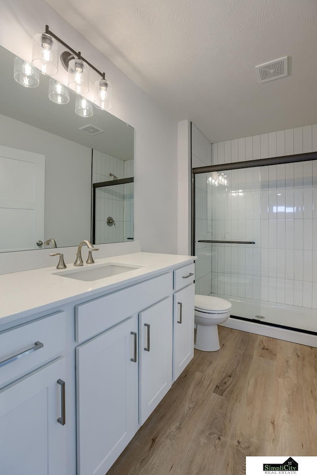 bathroom with wood finished floors, a stall shower, toilet, vanity, and a textured ceiling