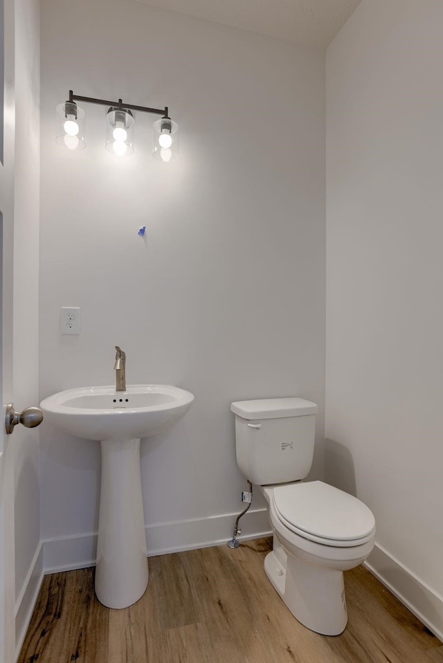 half bath with wood finished floors, baseboards, and toilet
