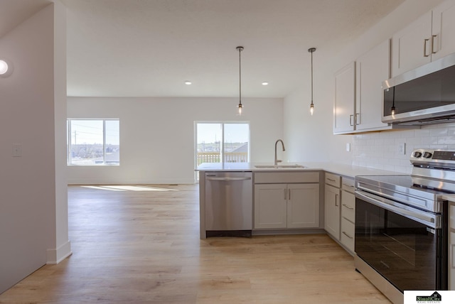 kitchen featuring stainless steel appliances, a sink, a peninsula, light wood-style floors, and recessed lighting