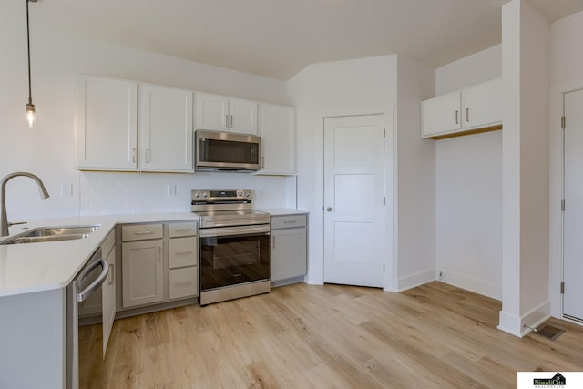 kitchen with appliances with stainless steel finishes, a sink, light wood finished floors, light countertops, and tasteful backsplash