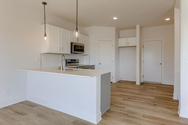 kitchen with appliances with stainless steel finishes, a sink, a peninsula, light countertops, and white cabinetry
