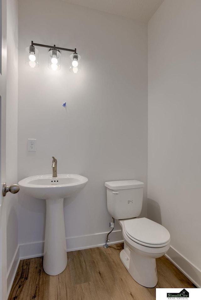half bath with wood finished floors, toilet, and baseboards