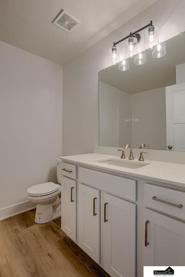 bathroom featuring wood finished floors, toilet, vanity, a textured ceiling, and baseboards