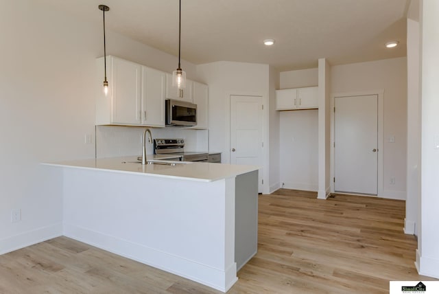 kitchen with stainless steel appliances, a sink, a peninsula, light countertops, and light wood-style floors
