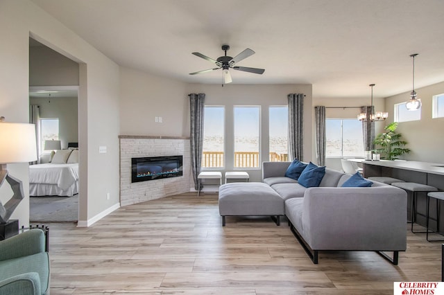 living room featuring ceiling fan, a chandelier, a glass covered fireplace, and light wood-style floors