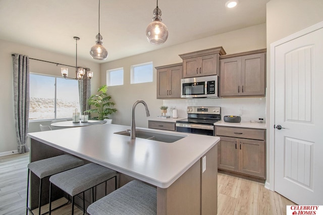 kitchen featuring appliances with stainless steel finishes, a sink, a kitchen island with sink, light wood finished floors, and a chandelier