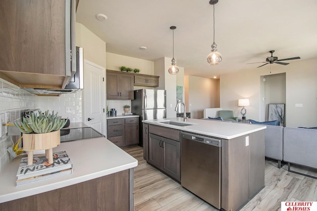 kitchen featuring a sink, appliances with stainless steel finishes, open floor plan, decorative backsplash, and light wood finished floors