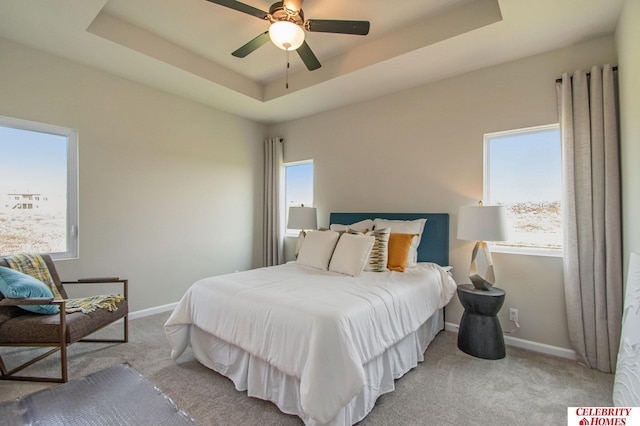 carpeted bedroom featuring baseboards, a raised ceiling, and a ceiling fan