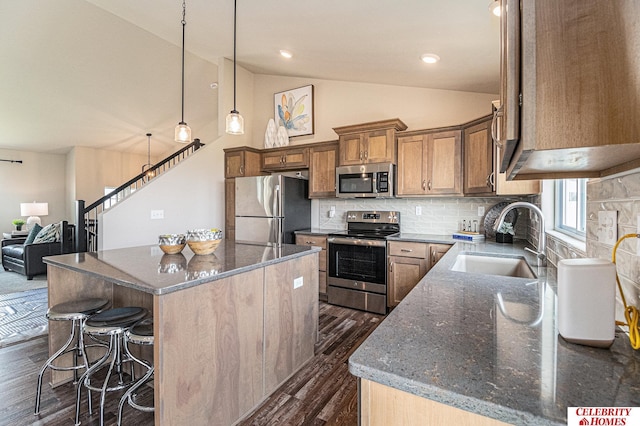 kitchen featuring stainless steel appliances, a sink, dark wood-type flooring, a center island, and vaulted ceiling