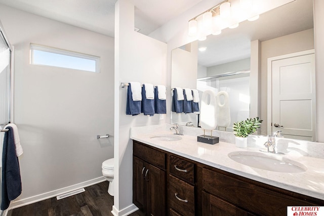 full bathroom with toilet, a shower stall, wood finished floors, double vanity, and baseboards