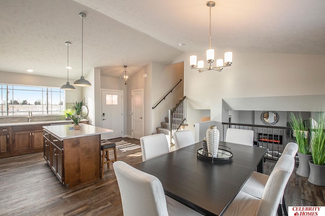dining space with stairway, dark wood finished floors, a chandelier, vaulted ceiling, and a tiled fireplace