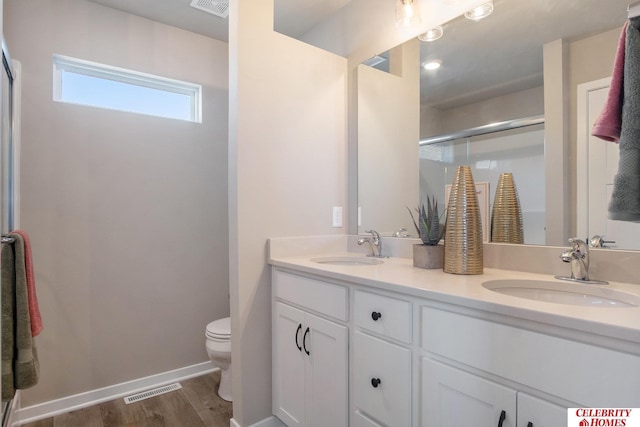 bathroom featuring toilet, a stall shower, double vanity, and wood finished floors