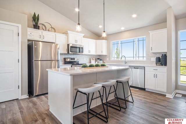 kitchen featuring stainless steel appliances, a kitchen island, white cabinetry, decorative backsplash, and vaulted ceiling