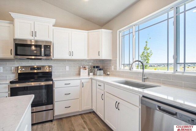 kitchen with appliances with stainless steel finishes, a sink, vaulted ceiling, backsplash, and white cabinetry