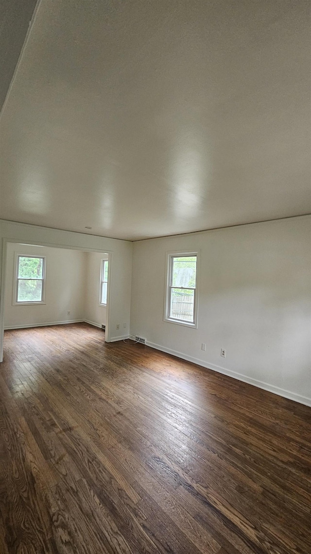 empty room featuring healthy amount of natural light, dark wood-style flooring, and baseboards