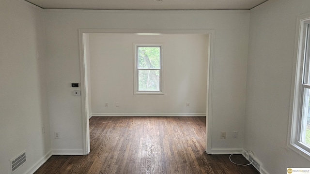 empty room with dark wood finished floors, healthy amount of natural light, and baseboards