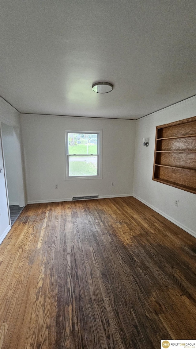 unfurnished room with wood finished floors, baseboards, built in shelves, baseboard heating, and a textured ceiling