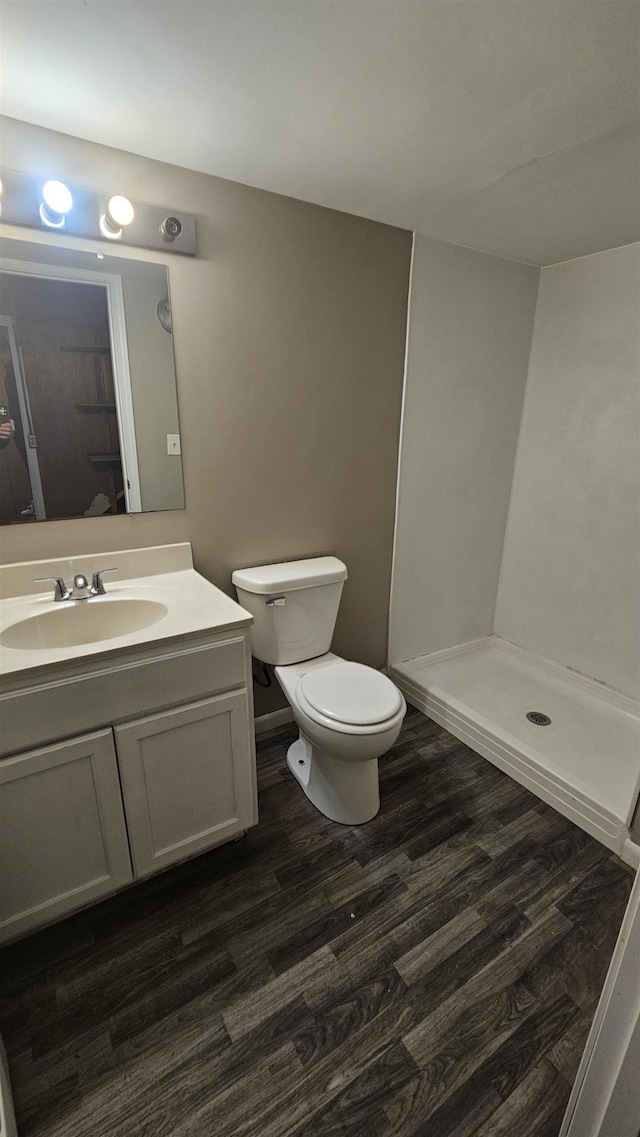 bathroom featuring wood finished floors, toilet, a shower stall, and vanity