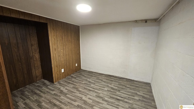 unfurnished bedroom with wood finished floors, wooden walls, and concrete block wall