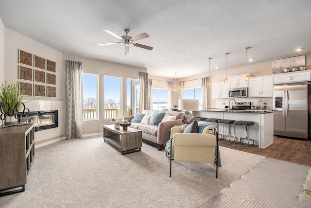 living area with ceiling fan, a glass covered fireplace, baseboards, and recessed lighting