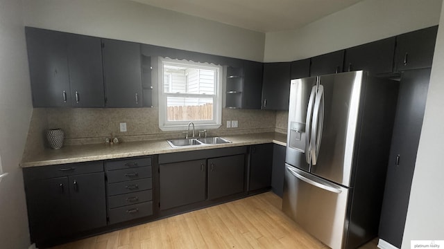 kitchen with stainless steel fridge with ice dispenser, a sink, light wood finished floors, and light countertops