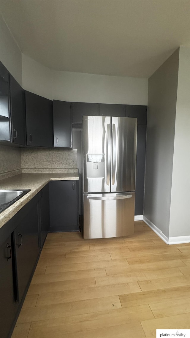 kitchen with stainless steel fridge, light wood finished floors, and dark cabinetry