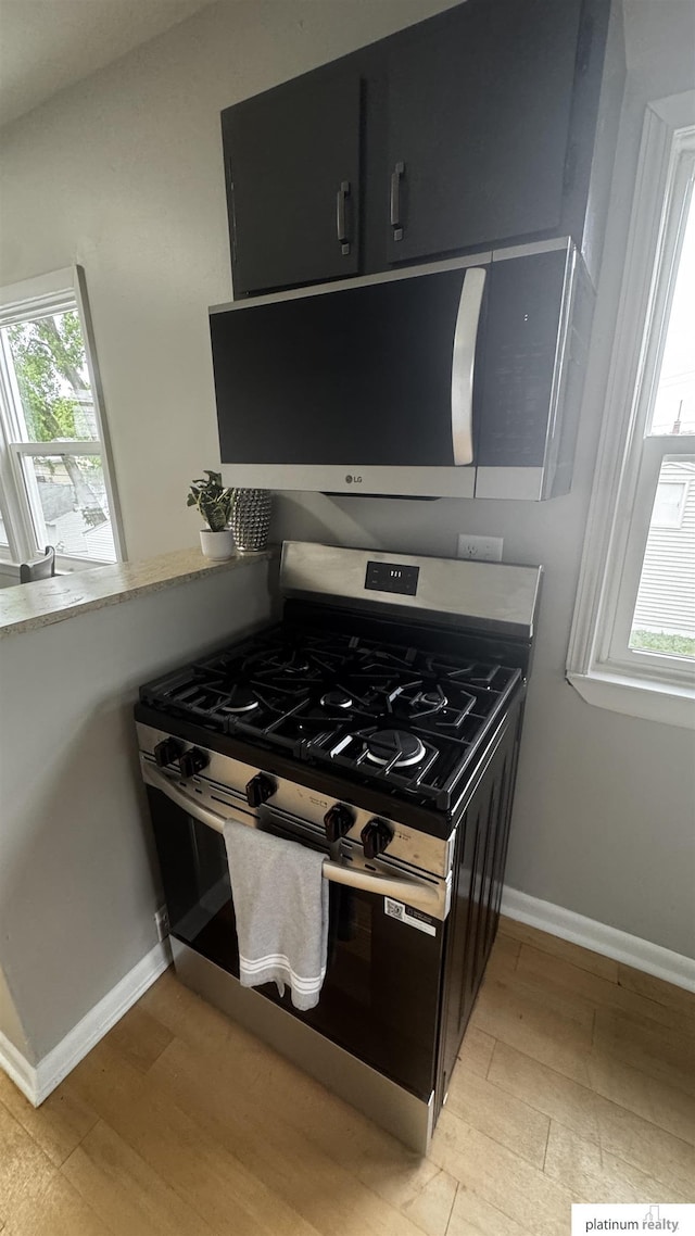 kitchen featuring stainless steel appliances, light wood-style floors, dark cabinets, and baseboards