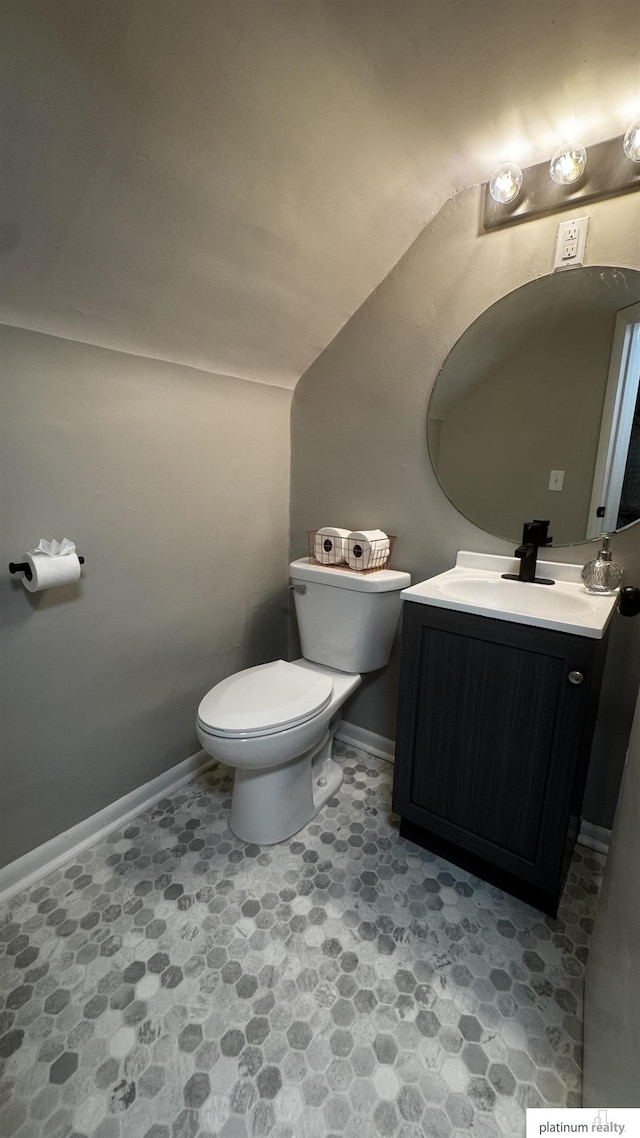 half bathroom featuring toilet, vanity, lofted ceiling, and baseboards