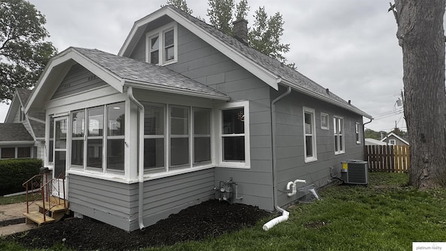 view of side of property featuring a chimney, a sunroom, roof with shingles, and central AC
