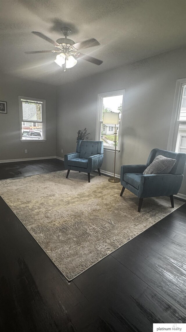 living area featuring baseboards, ceiling fan, a textured ceiling, and wood finished floors