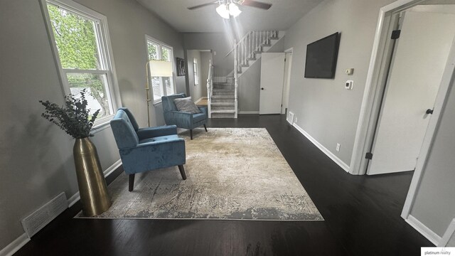 living area with a ceiling fan, dark wood-type flooring, baseboards, and stairway