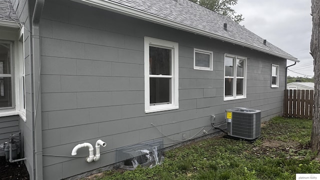 view of side of property featuring central AC unit and a shingled roof