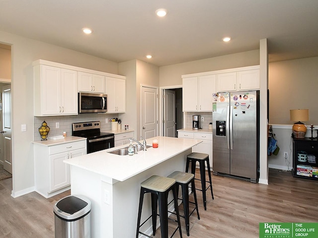 kitchen with appliances with stainless steel finishes, a sink, light wood finished floors, a kitchen breakfast bar, and tasteful backsplash