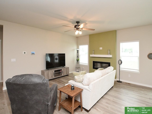 living area with a ceiling fan, a glass covered fireplace, light wood-type flooring, and baseboards